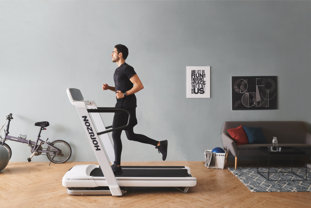 Mann auf Laufband der sein Lauftraining in seinem Wohnzimmer durchführt.