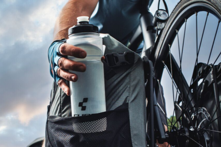 Radfahrer greift während der Fahrt zur Trinkflasche am Fahrrad, symbolisiert optimale Hydration und Flüssigkeitszufuhr für mehr Ausdauer und Leistung beim Sport