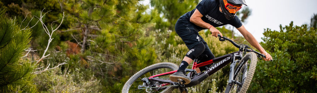 Mountainbike-Fahrer auf einem Trail mit wichtiger MTB-Ausrüstung für Einsteiger wie Helm, Protektoren und passende Bekleidung.