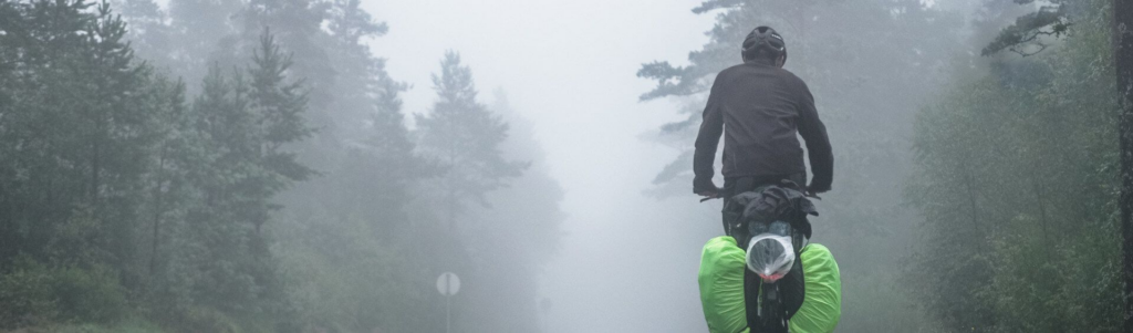 Bikepacker mit Fahrradtaschen fährt bei Nebel durch einen Wald – mehrtägige Bikepacking-Tour mit wetterfester Ausrüstung und Gepäck.