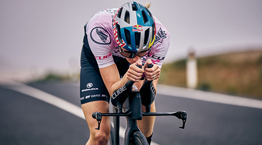 Aero-Rennrad. Im Bild sieht man eine Frau die am Auflieger vom Rennrad liegt und eine aerodynamische Position einnimmt 