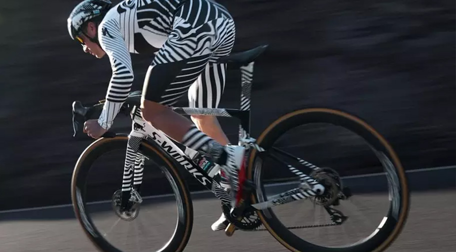 Ein Radsportler in einem schwarz-weiß gestreiften Zeitfahranzug fährt auf einem modernen Rennrad mit tiefen Carbon-Laufrädern. Durch die dynamische Fahrposition und die Bewegungsunschärfe der Umgebung entsteht der Eindruck einer schnellen Test- oder Trainingsfahrt.