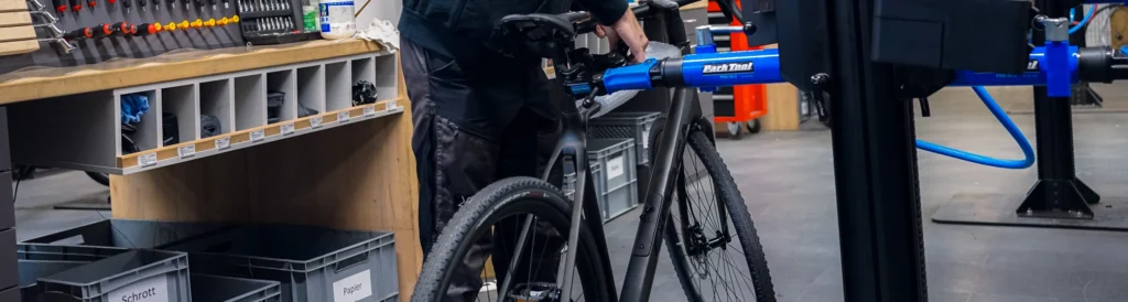 Auf dem Bild sieht man wie eine Person eine Fahrrad in einen Montageständer hängt um eine Reparatur durchzuführen.