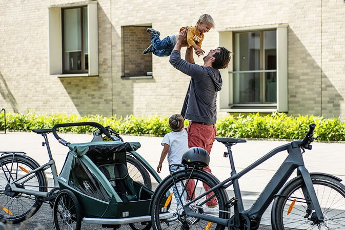 Elternteil mit Kinder und Kinderanhänger unterwegs auf einer Fahrradtour
