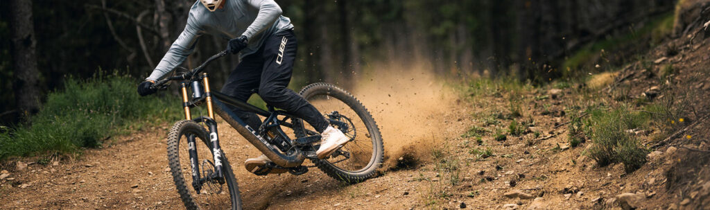 Mountainbiker fährt auf einem steinigen Trail durch den Wald und wirbelt dabei Staub auf.